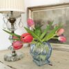 Art Deco Vase aus blauem Pressglas in Kugelform, bestückt mit roten Tulpen.. Die Vase steht neben einer antiken Lampe. Im Hintergrund ist ein Bild zu sehen.