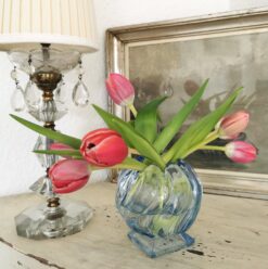 Art Deco Vase aus blauem Pressglas in Kugelform, bestückt mit roten Tulpen.. Die Vase steht neben einer antiken Lampe. Im Hintergrund ist ein Bild zu sehen.