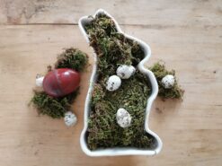 Alte Puddingform Hase, ausgekleidet mit Moos. Im Moosbett liegen Wachteleier. Neben der alten Keramikform sind Mooskissen sowie Wachteleier und eine alte Dose aus Blech in Ei-Form.