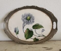 Antikes Jugendstil Tablett mit Blumen auf Keramikplatte. Das Tablett lehnt an der Wand.
