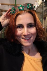 Portrait Selma Kürten-Kreibohm: lacht in die Kamera und hält eine antike Metallkrone über ihren Kopf.