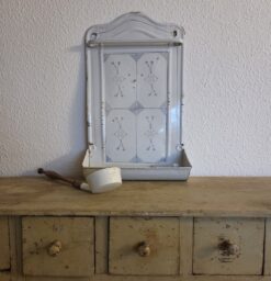 Antikes Emaille Kellenblech mit Strohblumendekor auf Schubladenschrank. Neben dem Löffelblech liegt eine Kelle.
