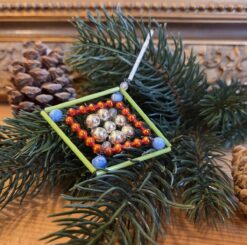 Vintage Gablonzer Christbaumschmuck in Rautenform: hellgrüne lange Stabperlen bilden eine Raute, in der wiederum eine Raute aus kleinen orangeroten Perlstäben ist. Im Zentrum sind Silberperlen zu einer Blume geformt. In den Ecken der äußeren Raute sind weiß-blau marmorierte Perlen.