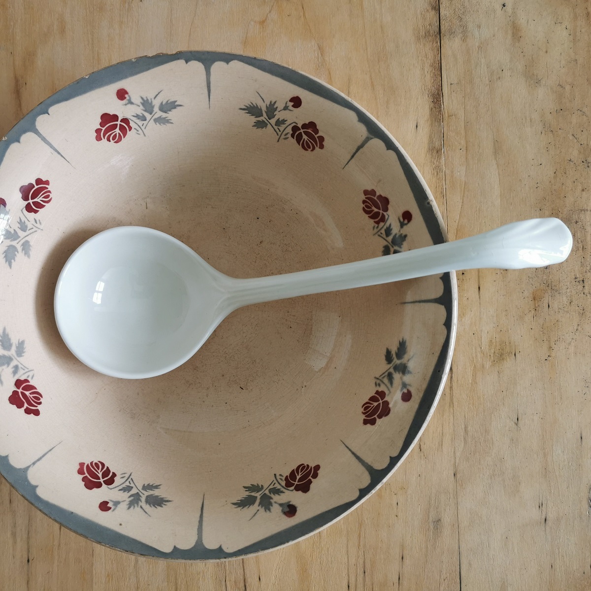 Alte cremeweiße Keramik-Suppenkelle in antiker zartrosa Keramikschüssel, die am Rand mit Blüten verziert ist.